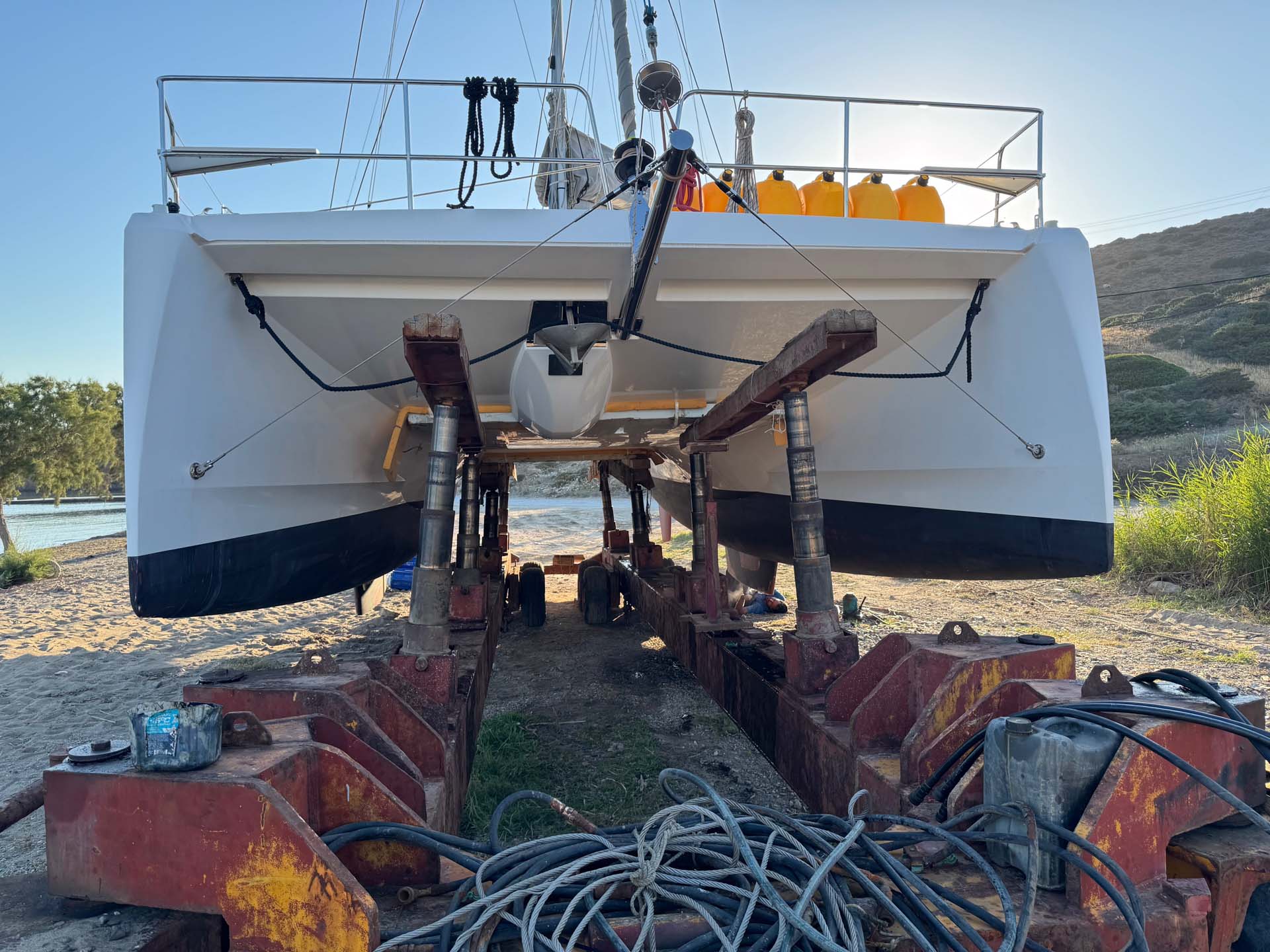 2026-06-06 Astypalea Schinunta Katamaran wird am Strand repariert. Der Carello mit Hydraulikstempeln hält ihn in der Höhe.