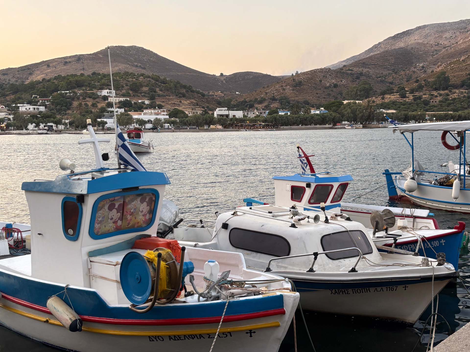 2026-07-20 Leros Xirokampos Boote im Fischehafen, Aloni gegenüber und darüber immer noch Rauch zu sehen